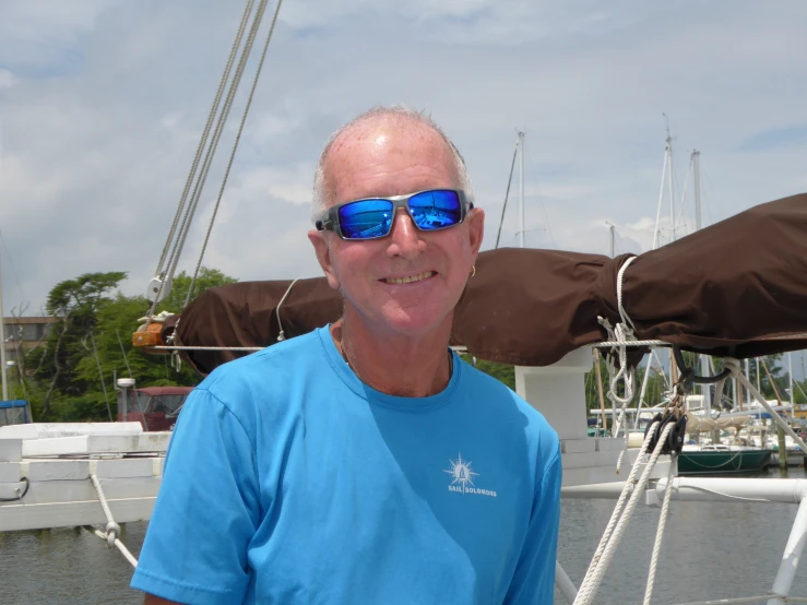 a man standing on the back of a sail boat wearing sunglasses