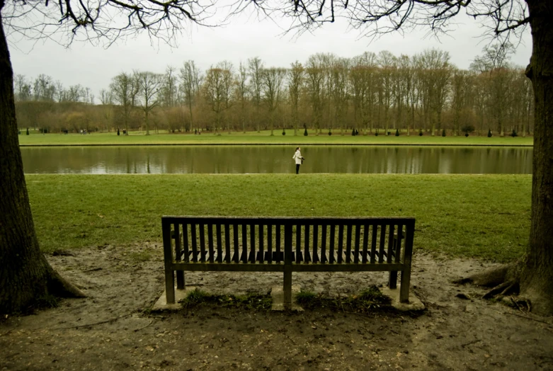 someone in the distance running away from a lake and a bench