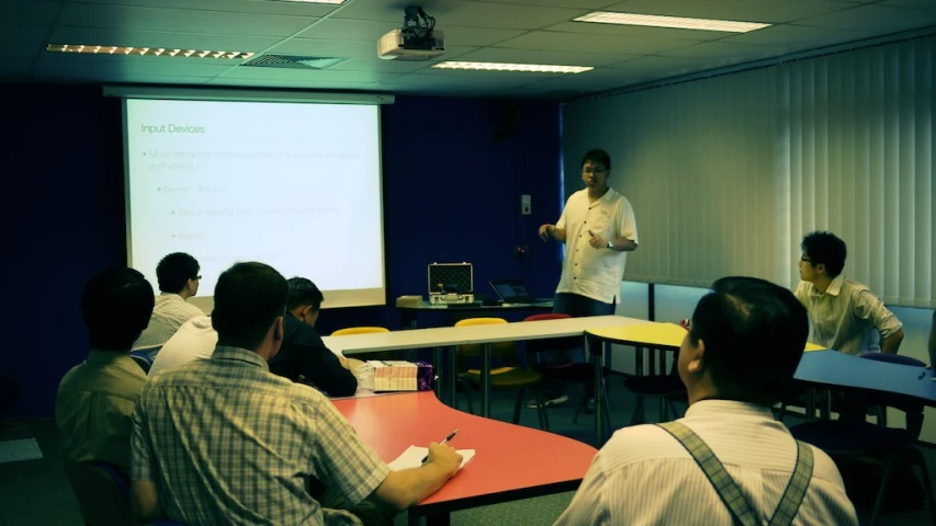 a man teaching at an office class in front of a group of men