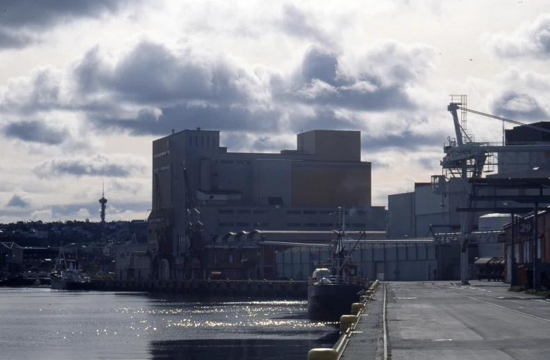 the river has boats docked and the power station is in the distance