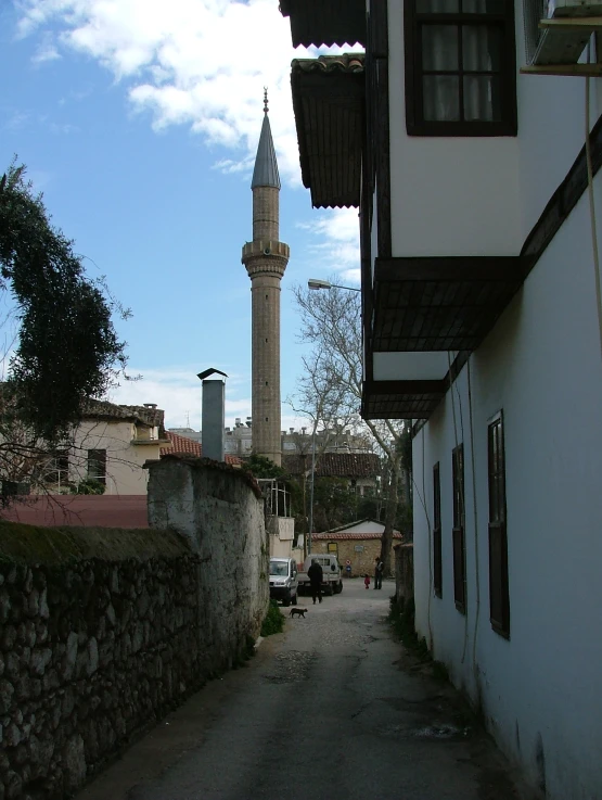 a narrow street has a small tower near the buildings