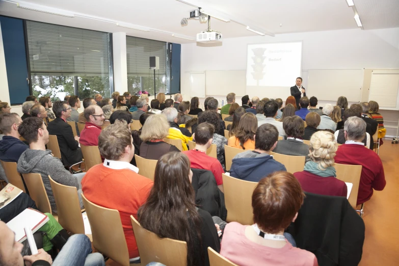 a large crowd in an auditorium listening to a man speaking