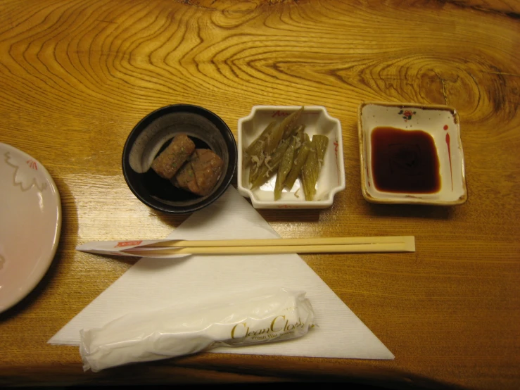 an arrangement of small containers with chopsticks and a bowl of sauce next to them on a wood table