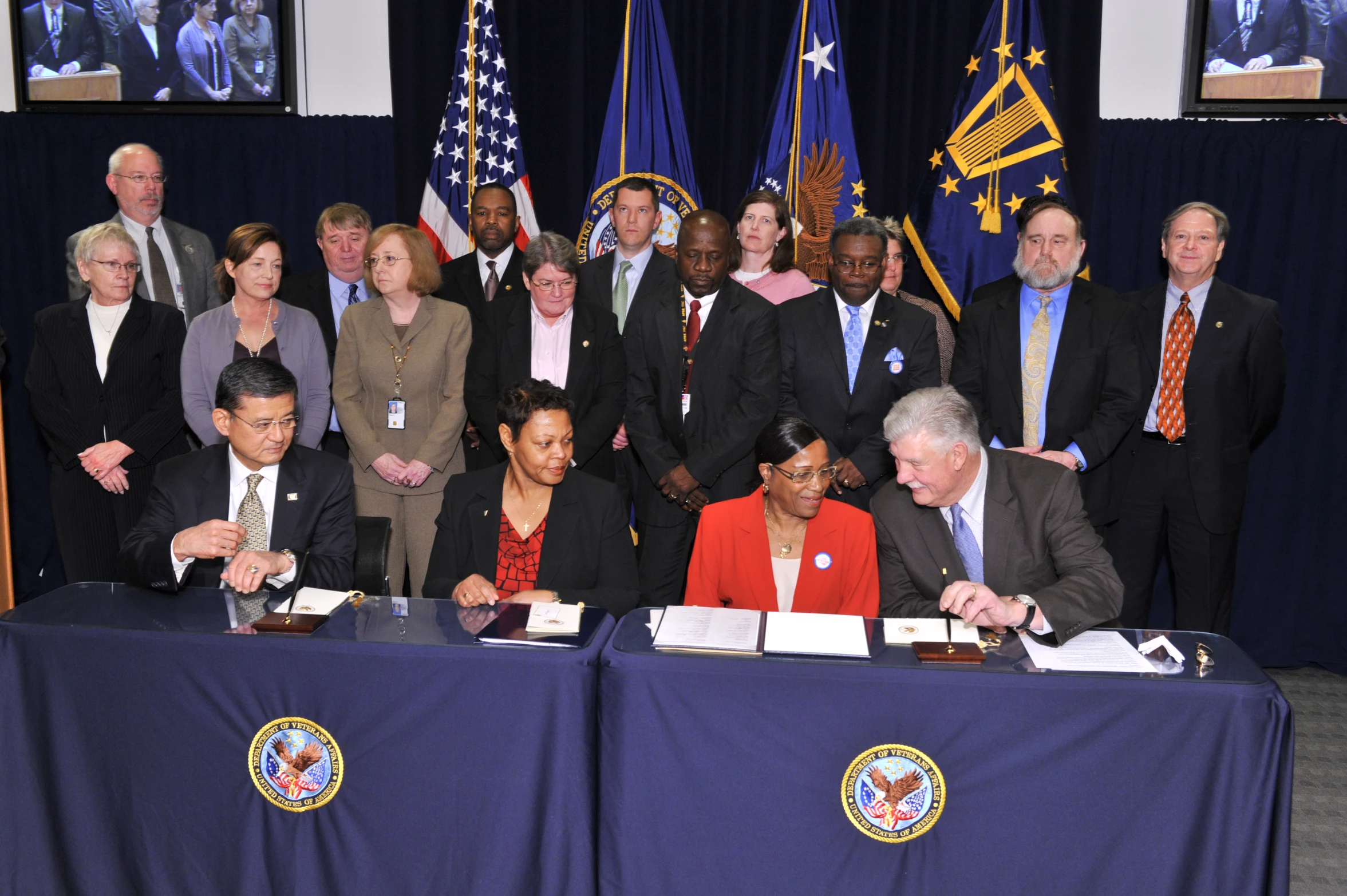 group of people standing behind a table signing papers