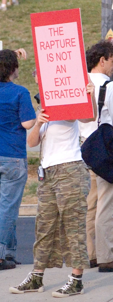 a man in camouflage pants holds up a sign saying the rapture is not an exit strategy