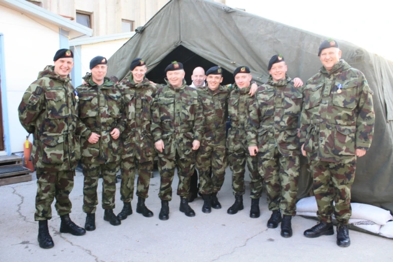 a group of men in camouflage standing in front of a tent