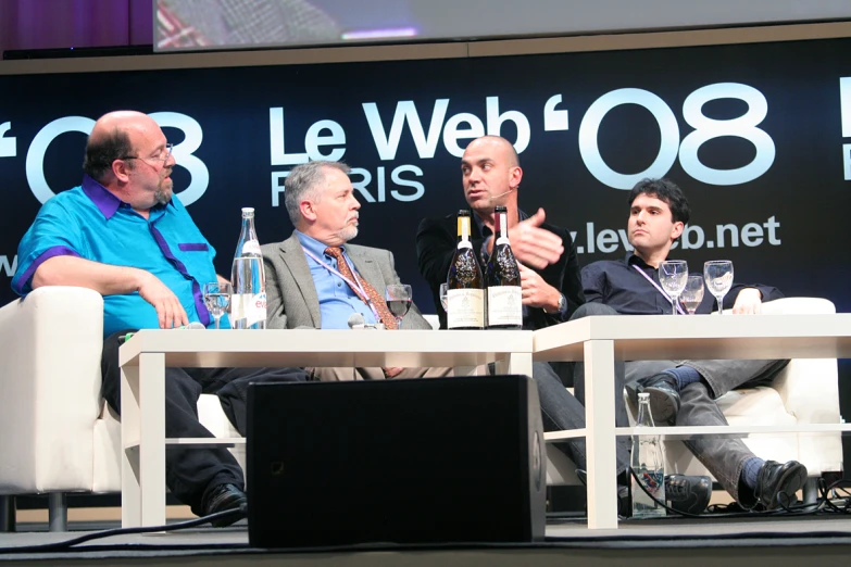 three men sit together on the stage talking to each other