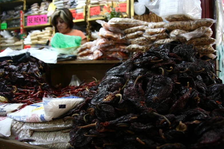 a woman sits behind a market with dried vegetables and other items