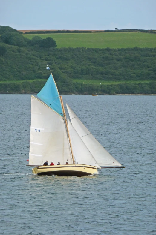 a sailboat floats along the water near an area with a green hill in the background