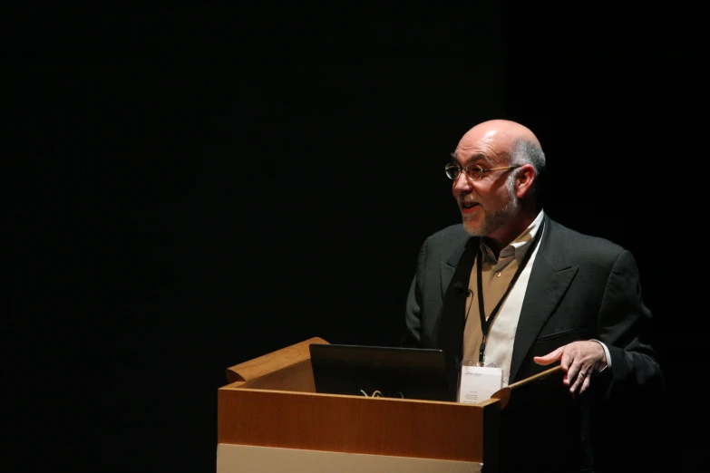 an old man standing in front of a podium with an electronic device