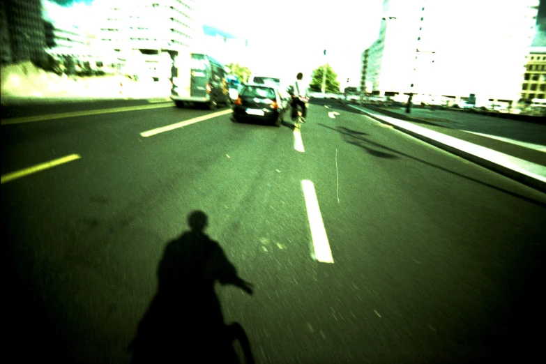 the shadow of the man riding a bike is cast by a car's headlights