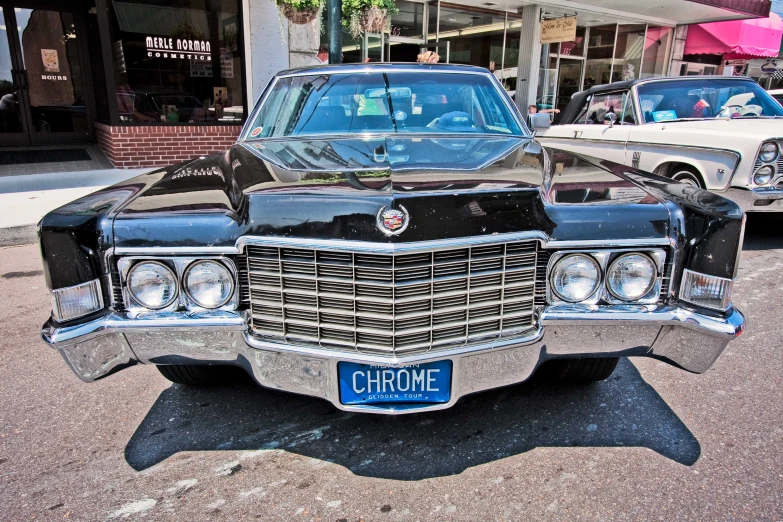 a chrome and black cadillac sits on the street in front of other classic cars