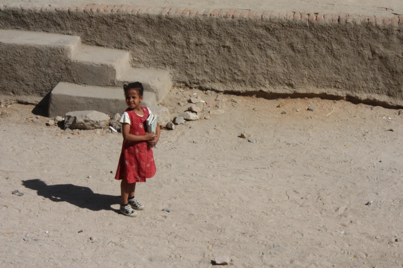 a little girl in a dress holding soing while standing in the sand