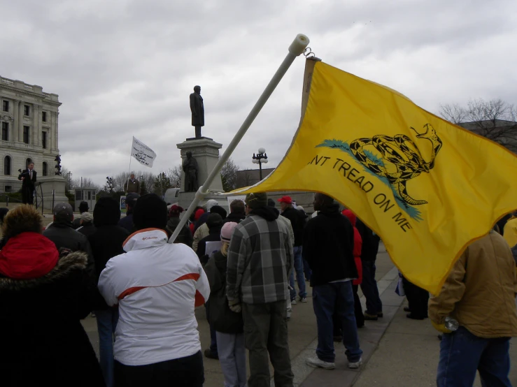 a group of people walking down the sidewalk next to a monument with a yellow flag in front of it