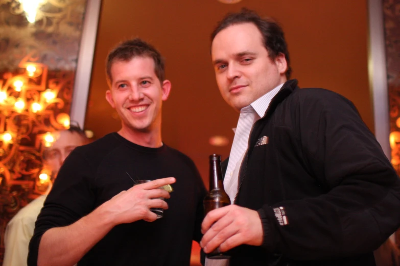 two men standing next to each other holding up beers