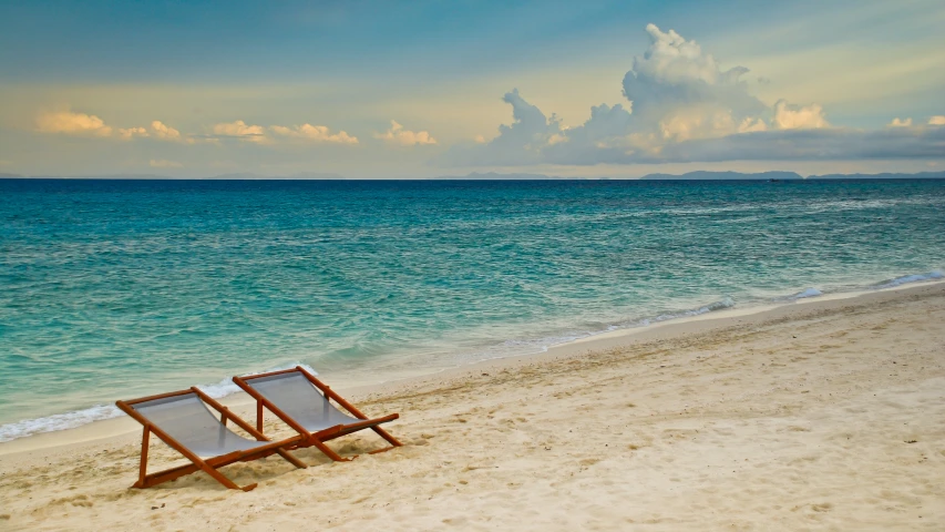 two chairs sit on the beach by the water