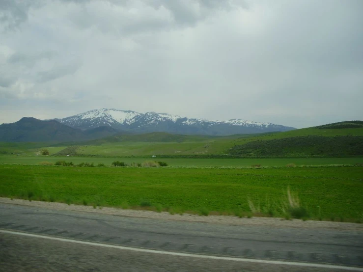 a road running through a field with snow - capped mountains