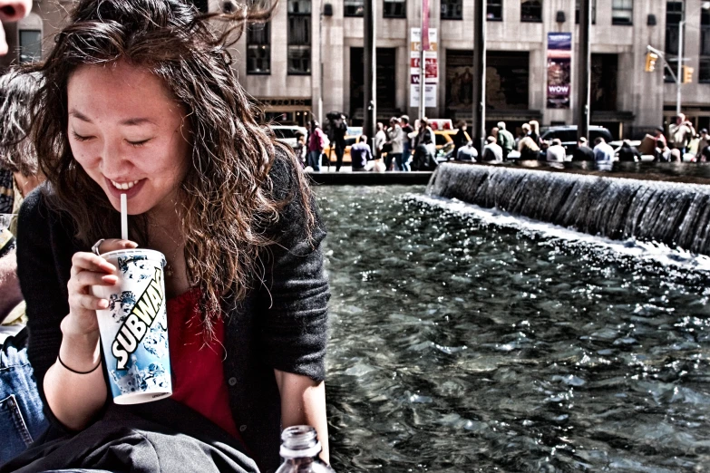 two women sitting and drinking sodas beside a fountain