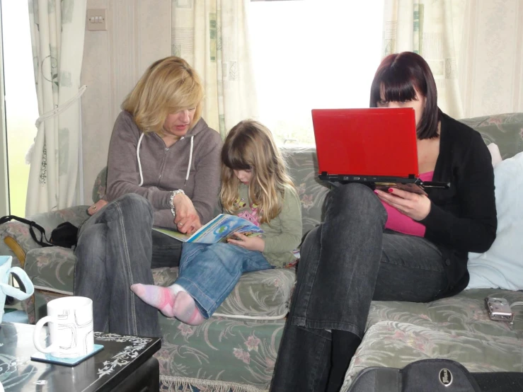 woman sitting on sofa with  holding book and other adult nearby reading