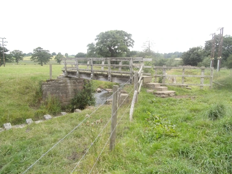 a fence is sitting next to a small creek and a road