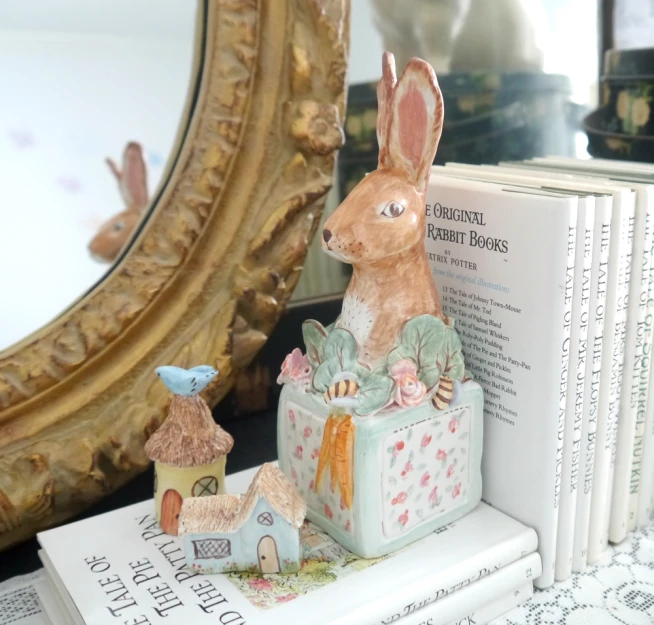 a small statue of a bunny rabbit sits on top of a box with other books behind it