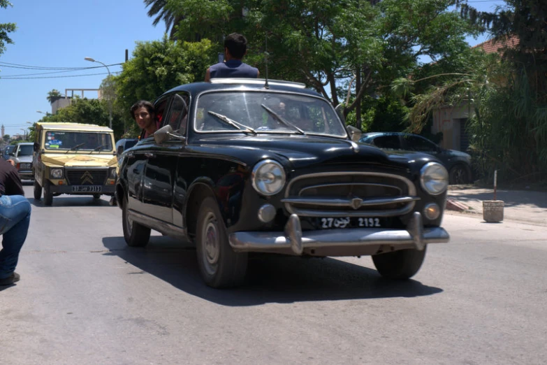 old fashioned car in street with two people riding in it