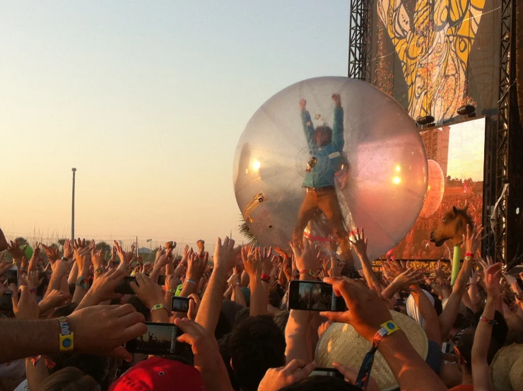 a crowd holds up large round balloons while another person pographs