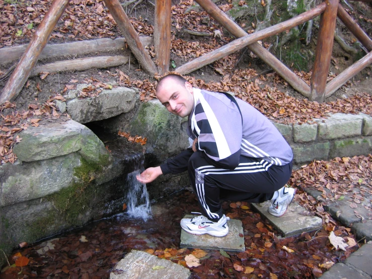 the man is crouching over looking at a pond