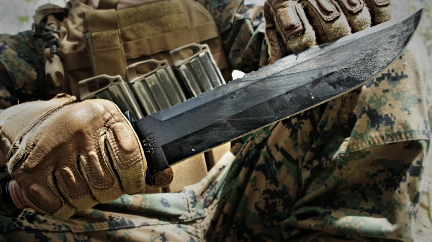 a person in military fatigues holds a large knife over their shoulders