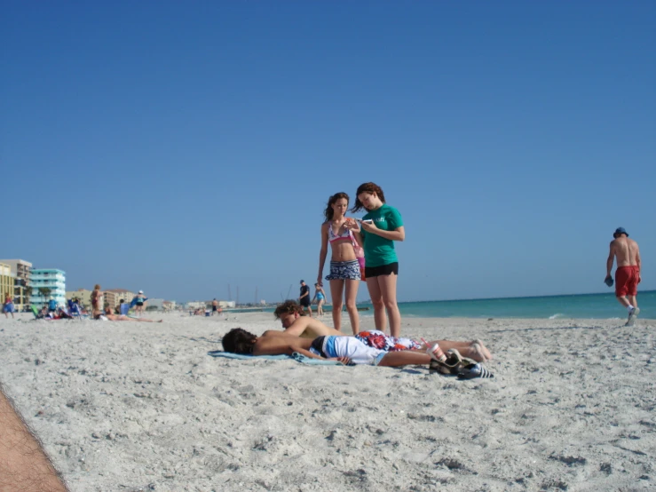 three people standing on the beach while one person lays down