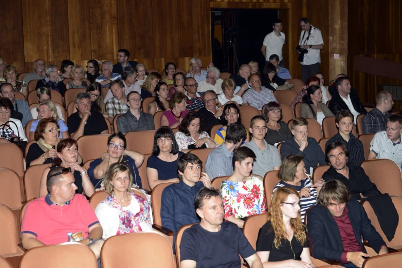 many people in rows watching an event and speaking