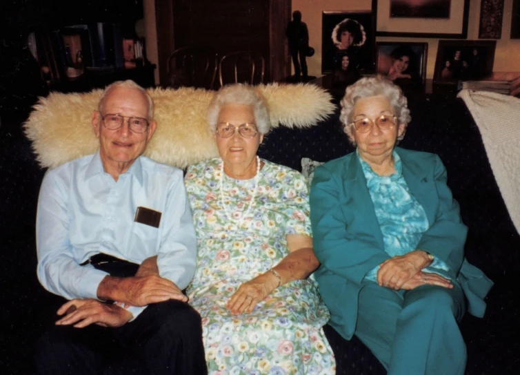 three older people are sitting on a black couch