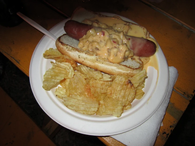 a plate topped with two  dogs covered in cheese and some potato chips