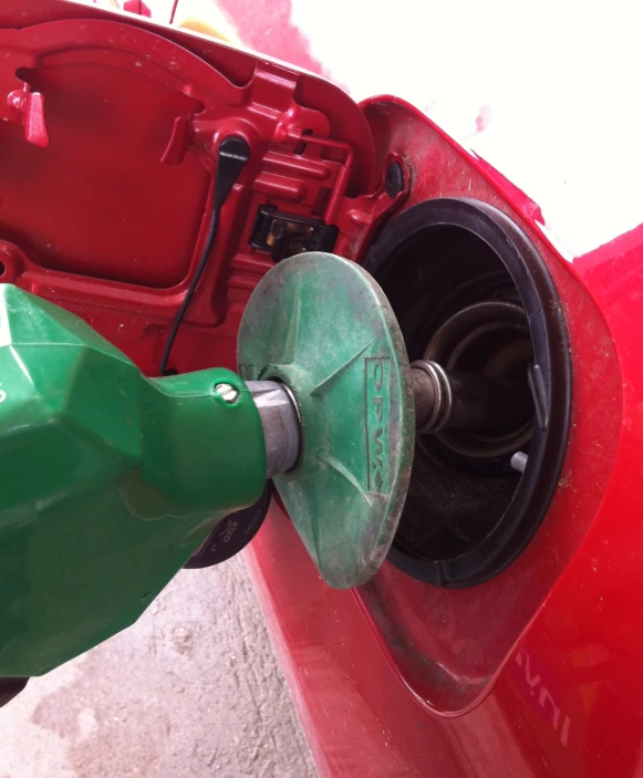 a red car has a fuel pump with green cap