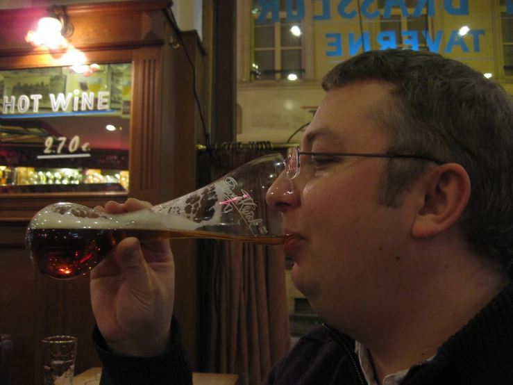 a man sipping a glass of wine near a neon sign