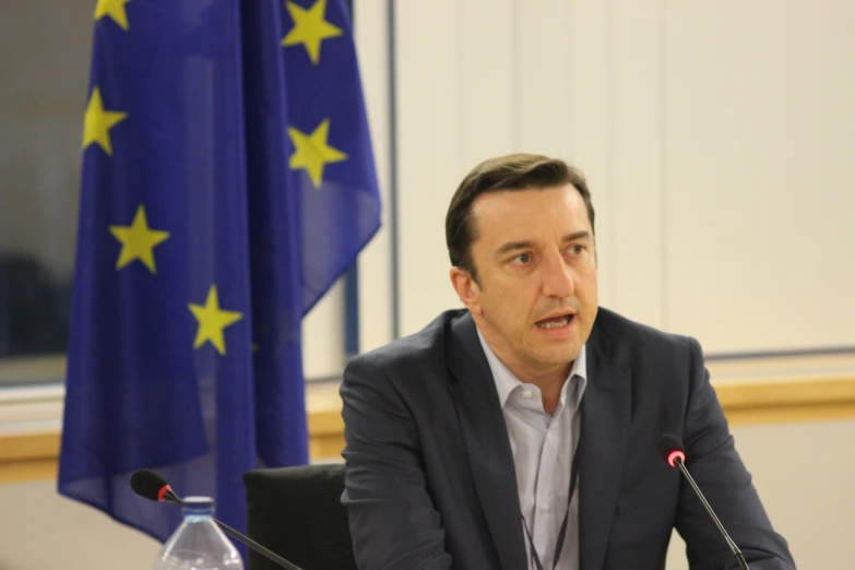 a man sitting at a table speaking in front of a microphone