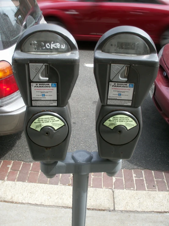 two parking meters on a side walk near parked cars