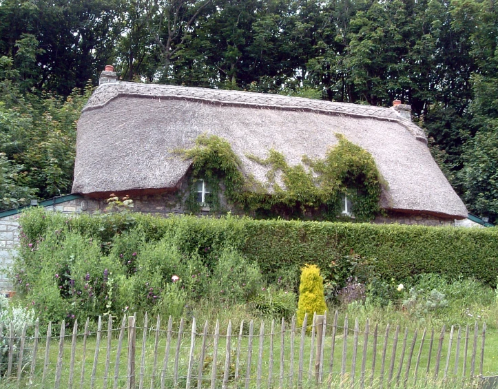 a large thatched roof house next to some trees and a fence