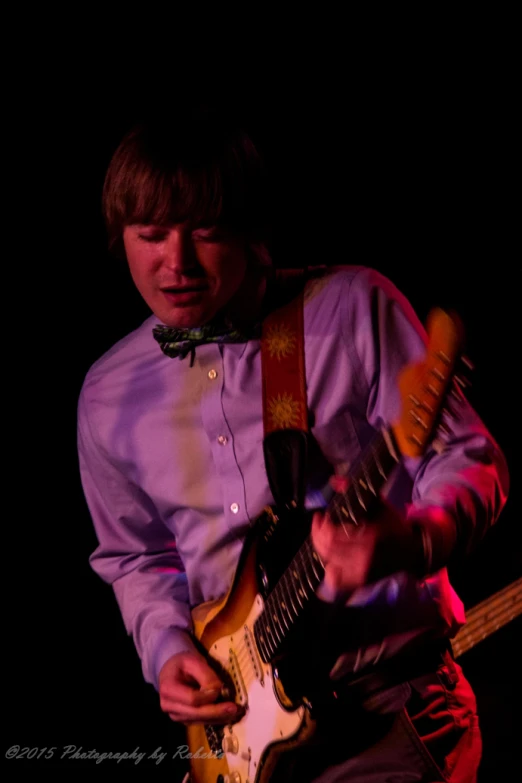 a man playing a guitar while wearing a bow tie