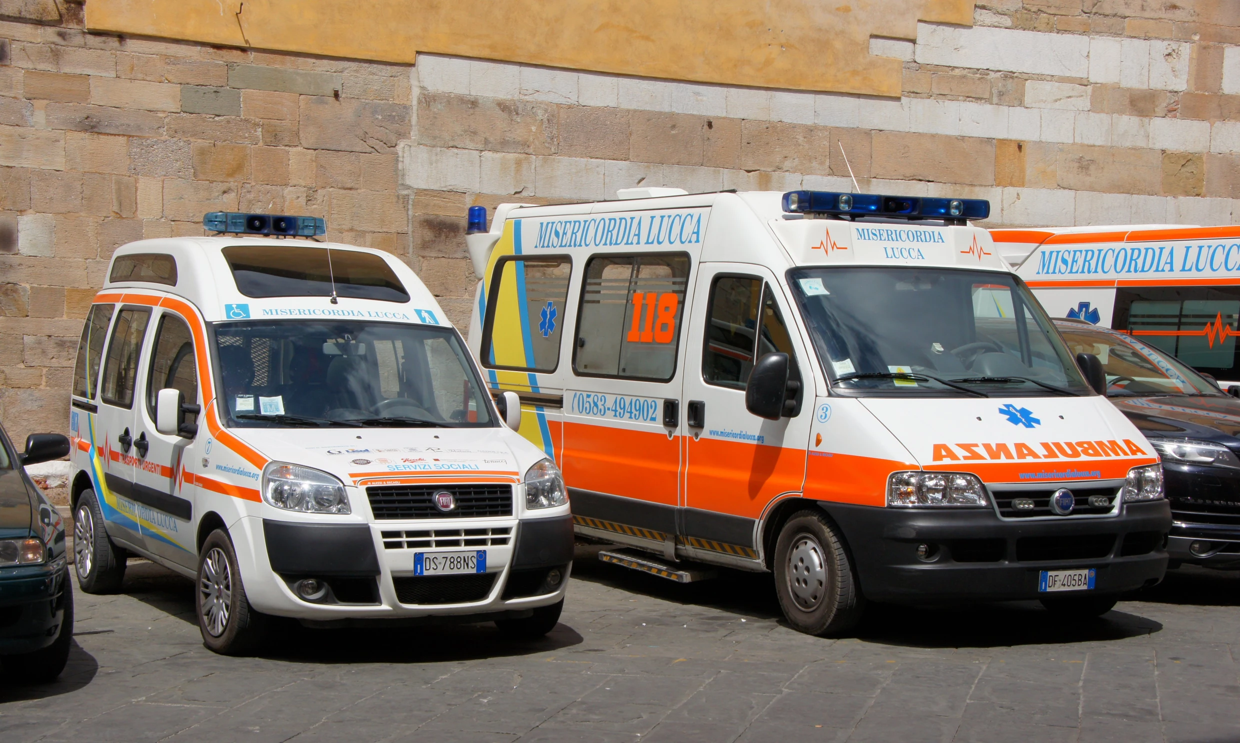 three parked ambulances are next to a stone wall