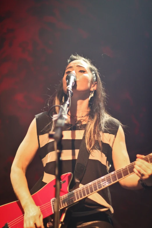 a female in black and white shirt singing and playing guitar