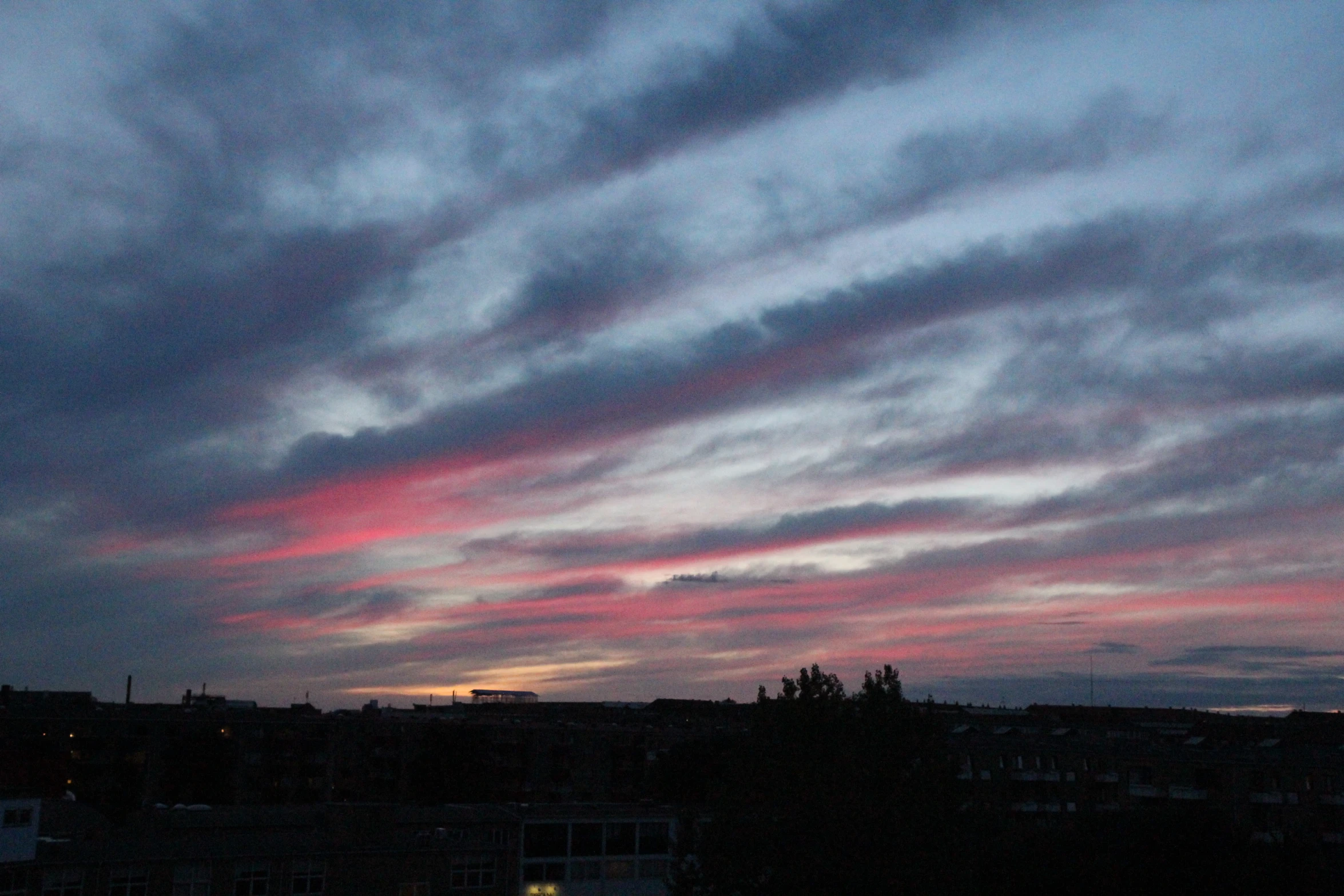 a sunset seen through clouds above houses in a city