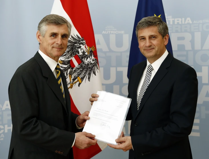 two men in business suits and one is holding up a document