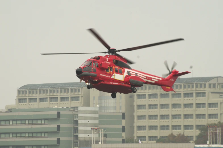 a red helicopter flying above the ground outside of some buildings