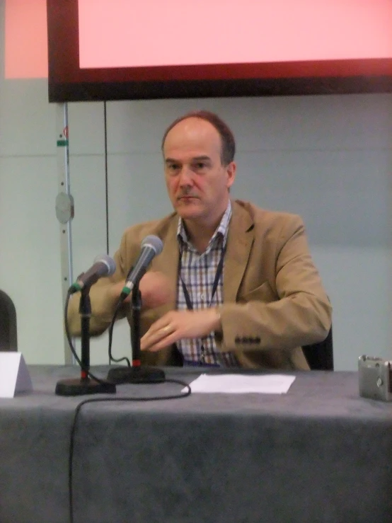 a man speaking into a microphone with a sign in the background