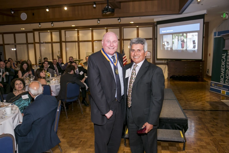 two men standing together in front of a large screen