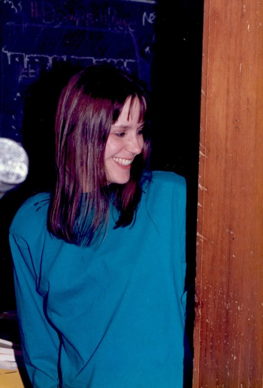 woman wearing a bright blue shirt smiles and leans against a wall