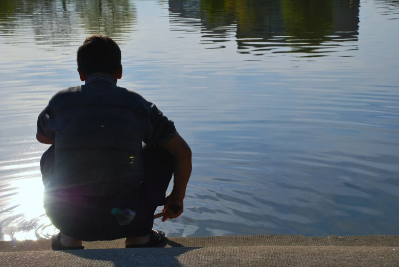 a man sitting on the shore by a lake looking at the water