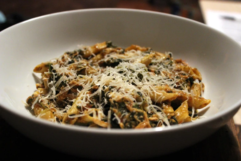 a white bowl with pasta topped with cheese and spinach