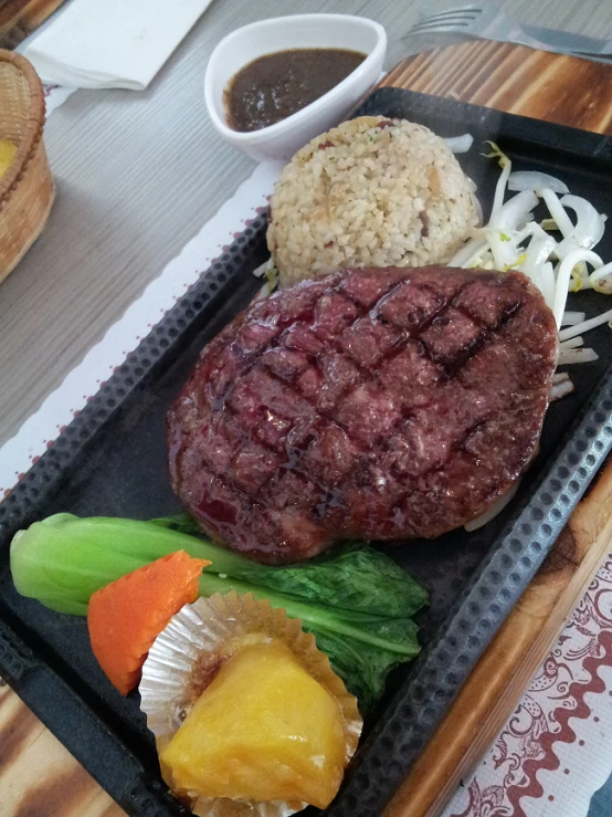 a steak with meat, sauce, and vegetables on a tray